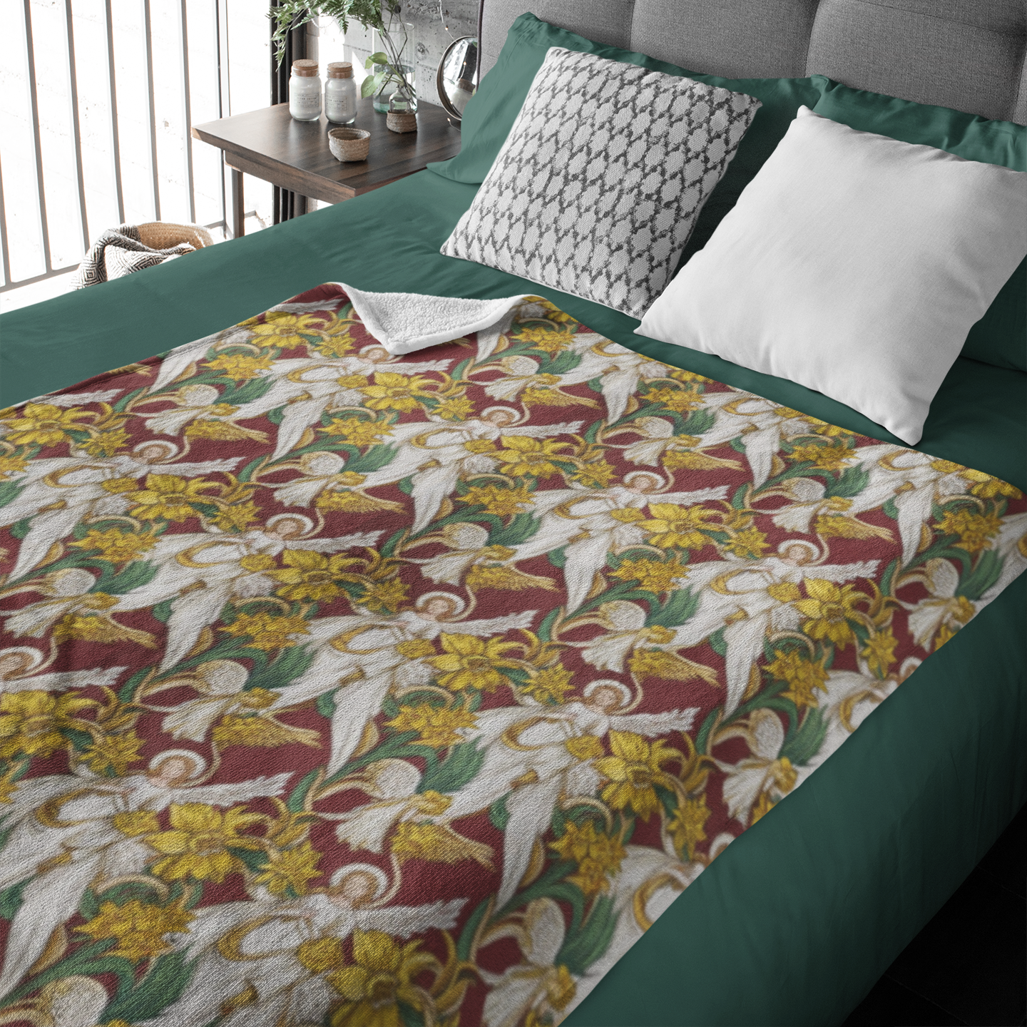 A cozy bed featuring a colorful blanket with a floral pattern in yellow, white, and green, draped over a green bedspread. Two decorative pillows, one patterned and one plain white, rest against a gray headboard.