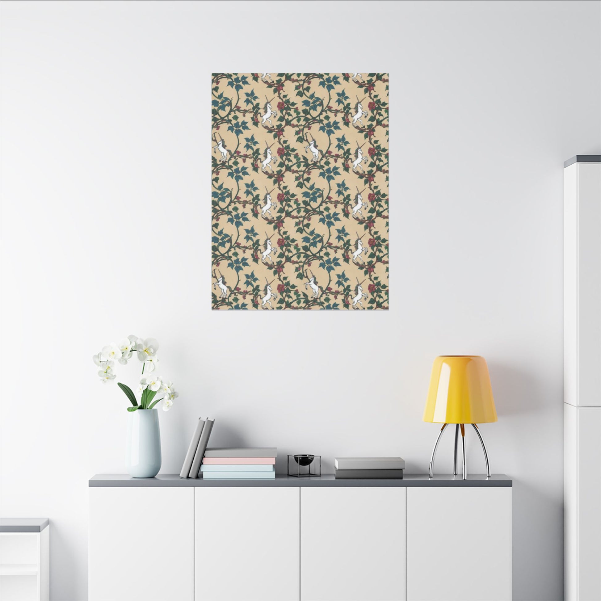 A patterned artwork hangs on a light wall, featuring white unicorns among green ivy and red flowers on a beige background. Below, a minimalist desk with a laptop and a small vase creates a stylish and inviting workspace.
