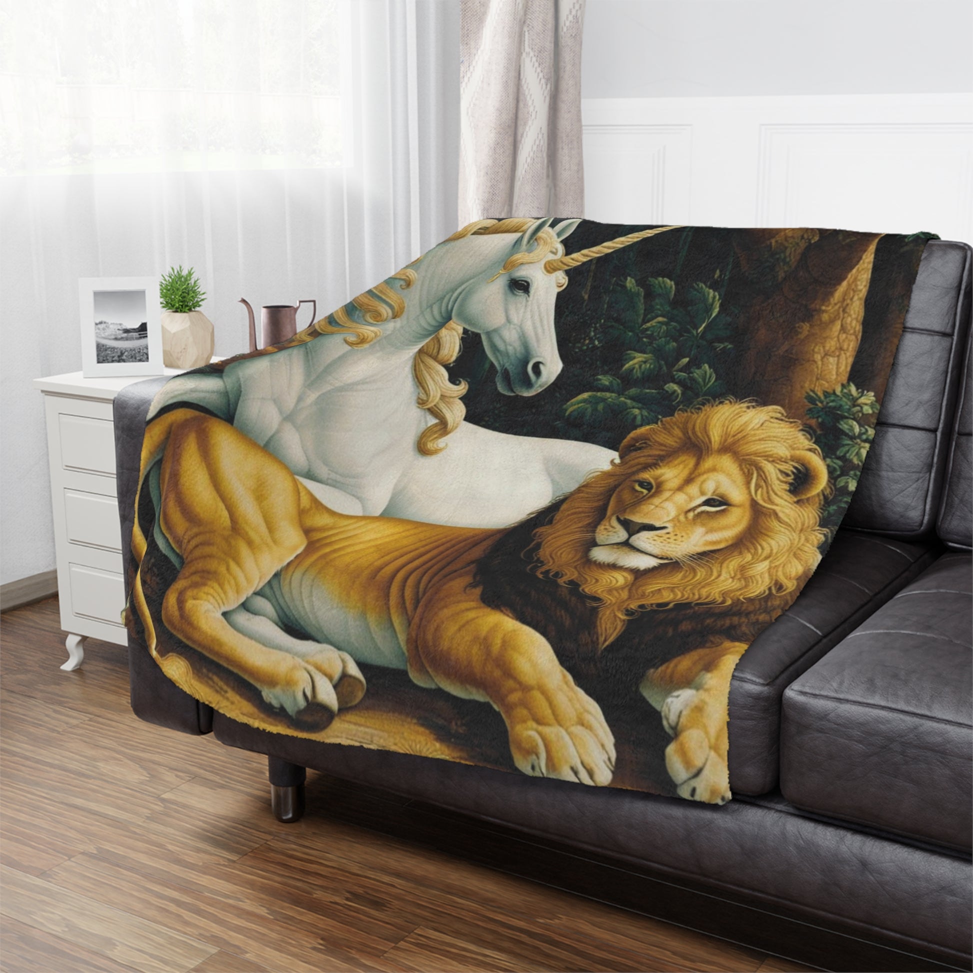 A cozy black leather couch features a blanket depicting a white unicorn and a golden lion resting together. A small plant and a decorative pitcher sit on a nearby white side table, with soft natural light streaming through the window.
