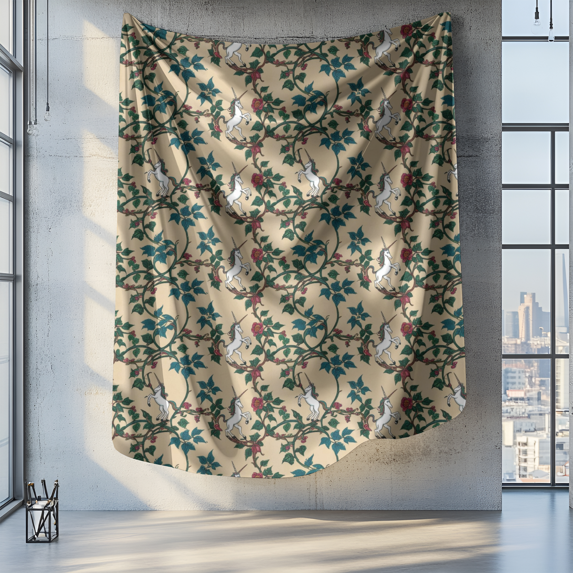 A patterned tapestry hangs against a concrete wall in a sunlit room. The design features white unicorns intertwined with green vines and red flowers on a beige background. Large windows beside it allow natural light to fill the space, highlighting the vibrant colors.
